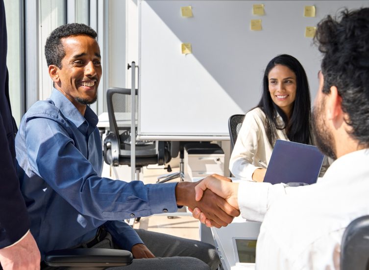 Diverse happy business men handshaking at group meeting. Male manager shaking hand of corporate client making partnership contract with investor at professional work team meeting in office.